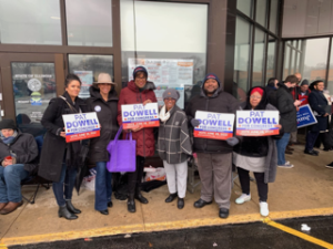 6 people (5 women, 1 man) stand in line holding "Pat Dowell for Congress" signs